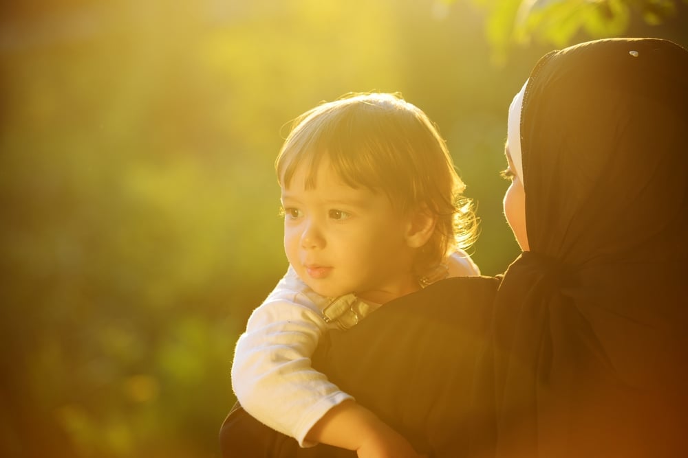 Middle Eastern Muslim mother playing with her little baby in green park and holding him in arms